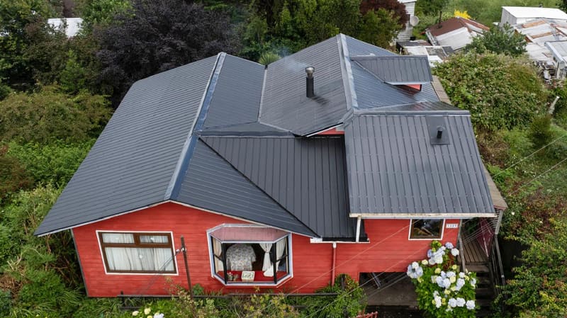 Casa roja con techumbre metálica gris recién instalada, vista desde el aire