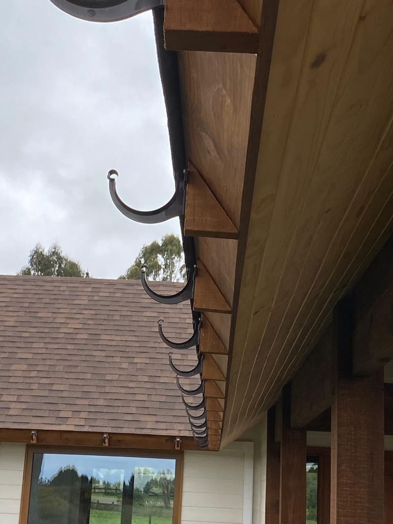 Detalle del alero de una casa: vigas de madera a la vista y ganchos de canal recién instalados