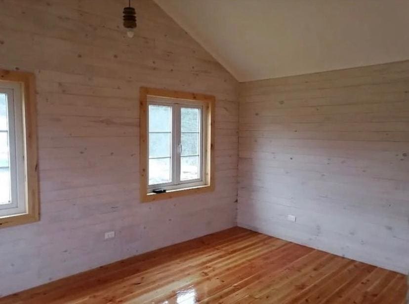 Dormitorio con paredes revestidas en madera clara y piso de pino barnizado